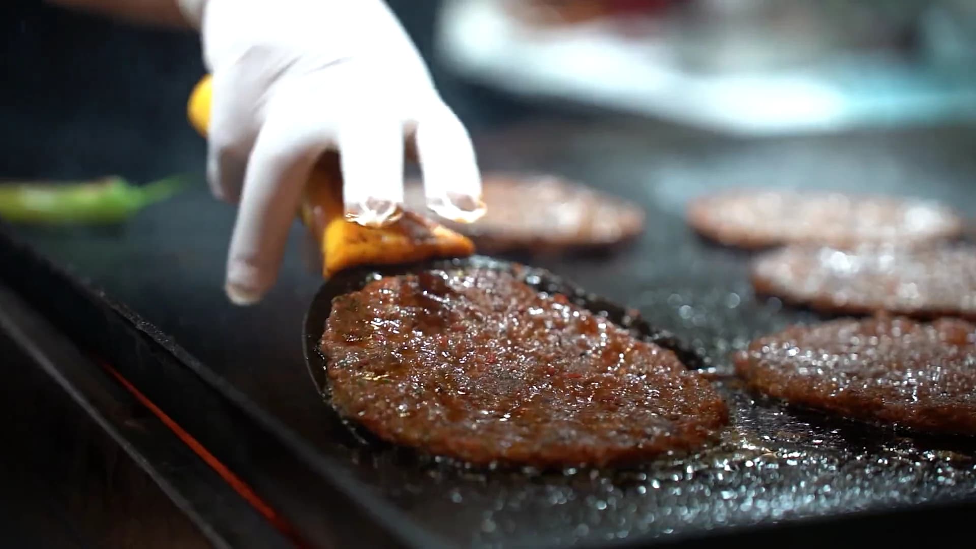 Smash-Patties brutzeln auf der dunklen Grillplatte, ein Wender drückt das vorderste Patty an